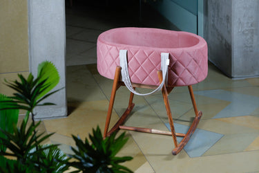 Pink baby crib with wooden legs on a tiled floor