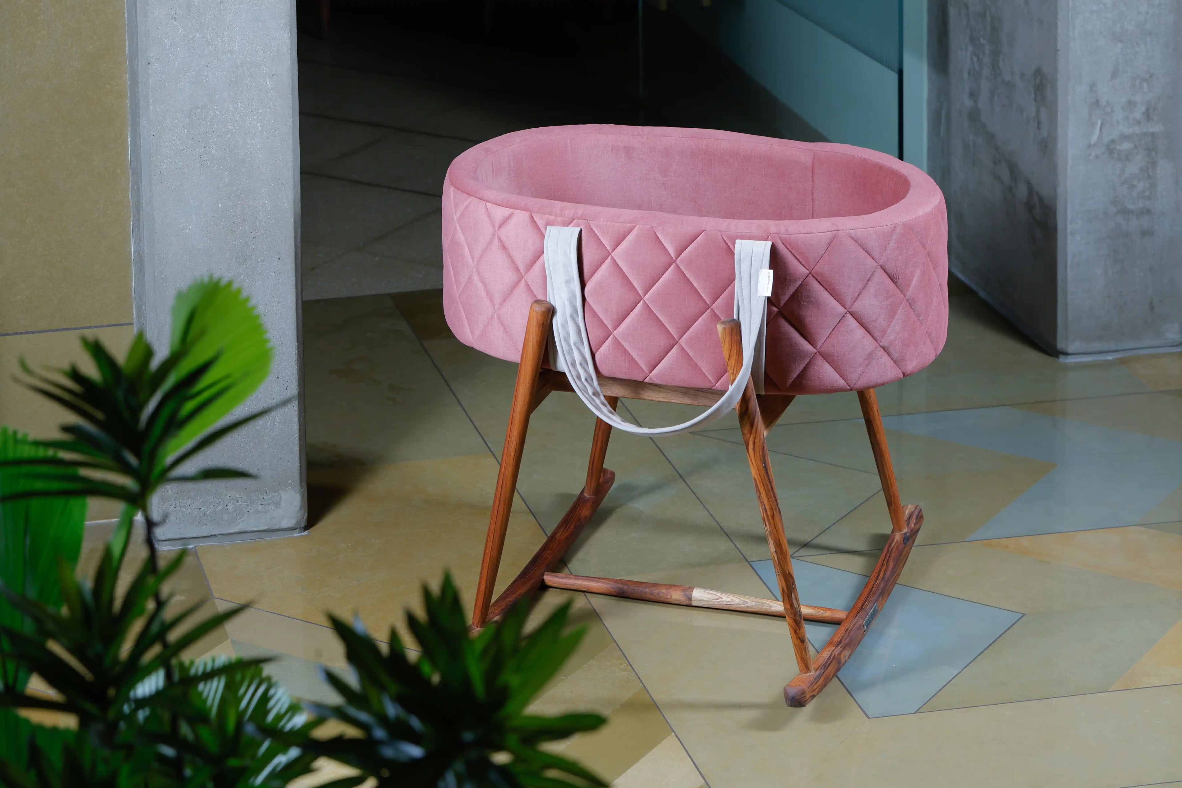 Pink baby crib with wooden legs on a tiled floor
