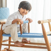 Child sitting on a wooden chair with a blue cushion
