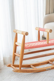 Wooden rocking chair with pink cushion in a room with white curtains