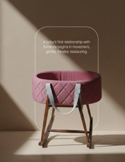 Pink baby bassinet on a wooden stand with a quote about babies' first relationship with furniture